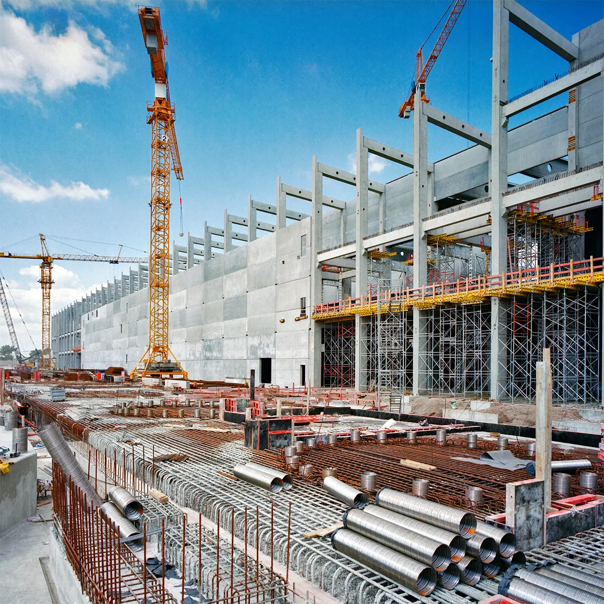 A large-scale construction site with cranes, scaffolding, and concrete structures in progress. Steel reinforcements and building materials are arranged, showcasing the industrial construction process. Prime Edge Technical Services LLC ensures precise construction survey solutions for efficient project execution.