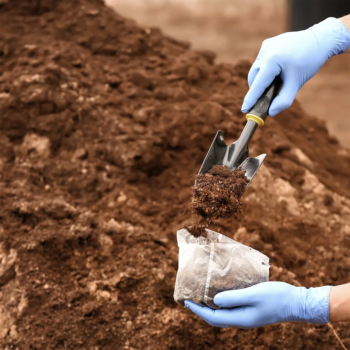 A professional conducting soil investigation, carefully collecting a soil sample with a trowel while wearing protective gloves. Prime Edge Technical Services LLC offers expert soil testing and analysis for construction and geotechnical projects.
